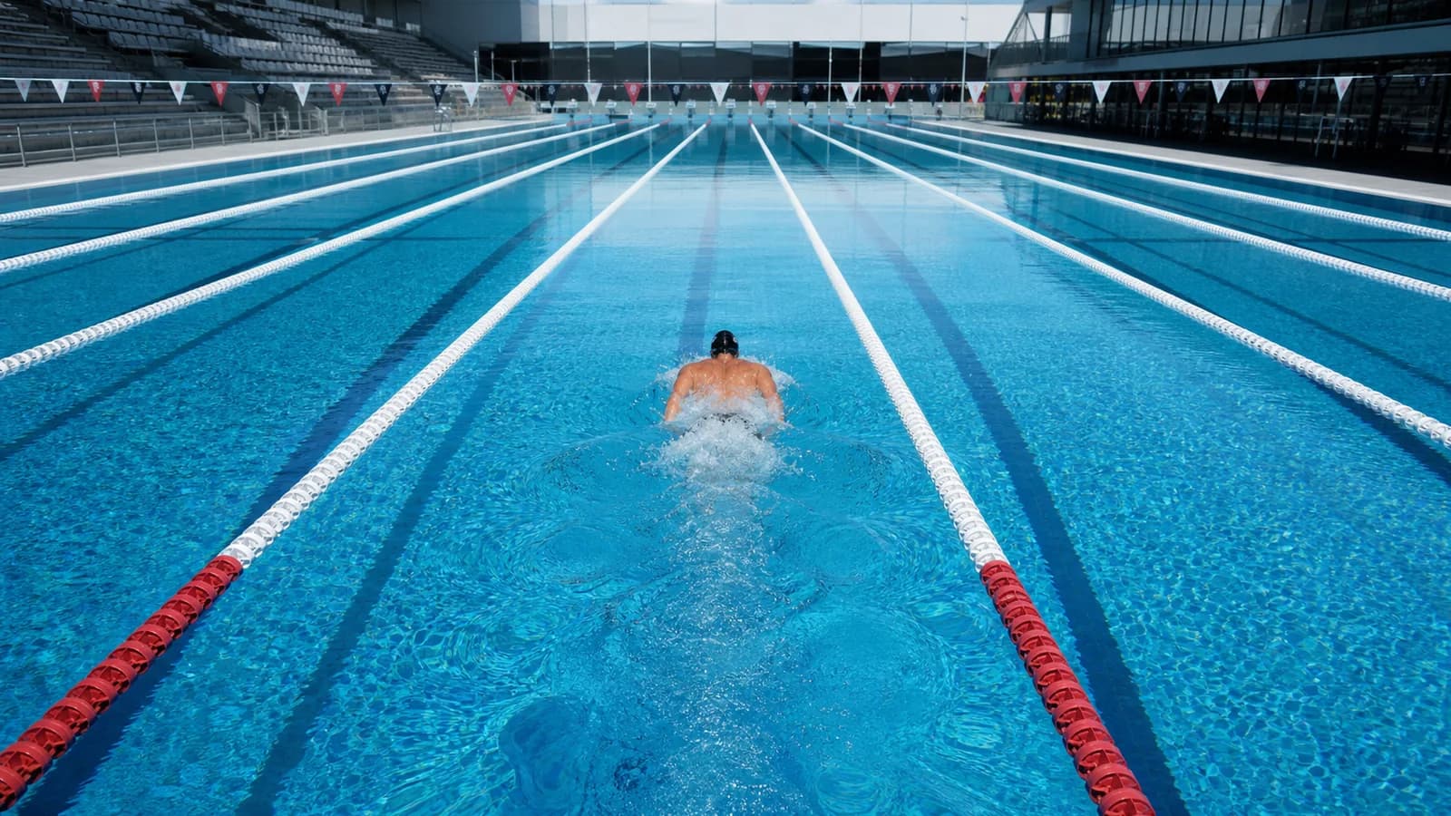 Nageur seul dans une ligne d'un grand bassin olympique lumineux.